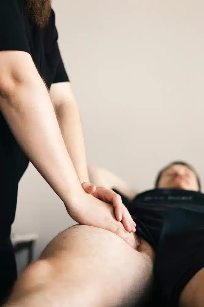 Masażysta wykonuje masaż nogi u leżącej klientki po wysiłku.